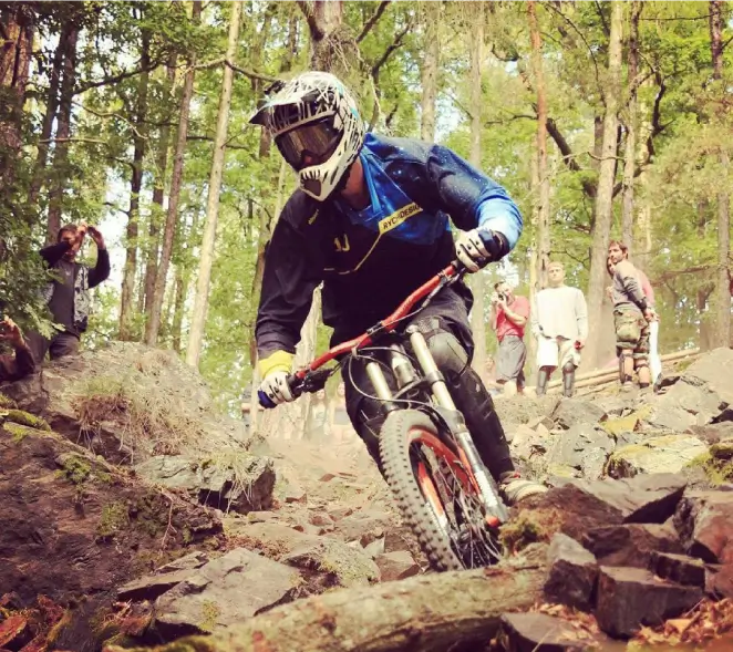 A downhill rider descending a rocky forest trail in a full-face helmet