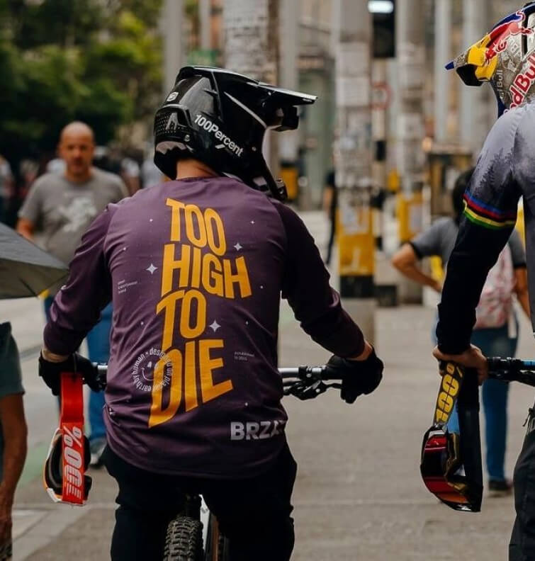 Rider seen from behind in a Too High To Die tee on a city street