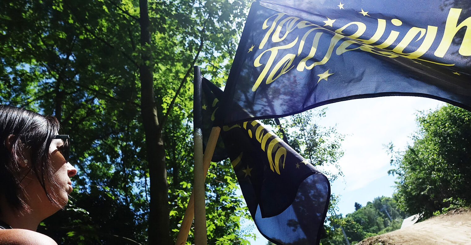 A Too High To Die flag waving by a forest bike track