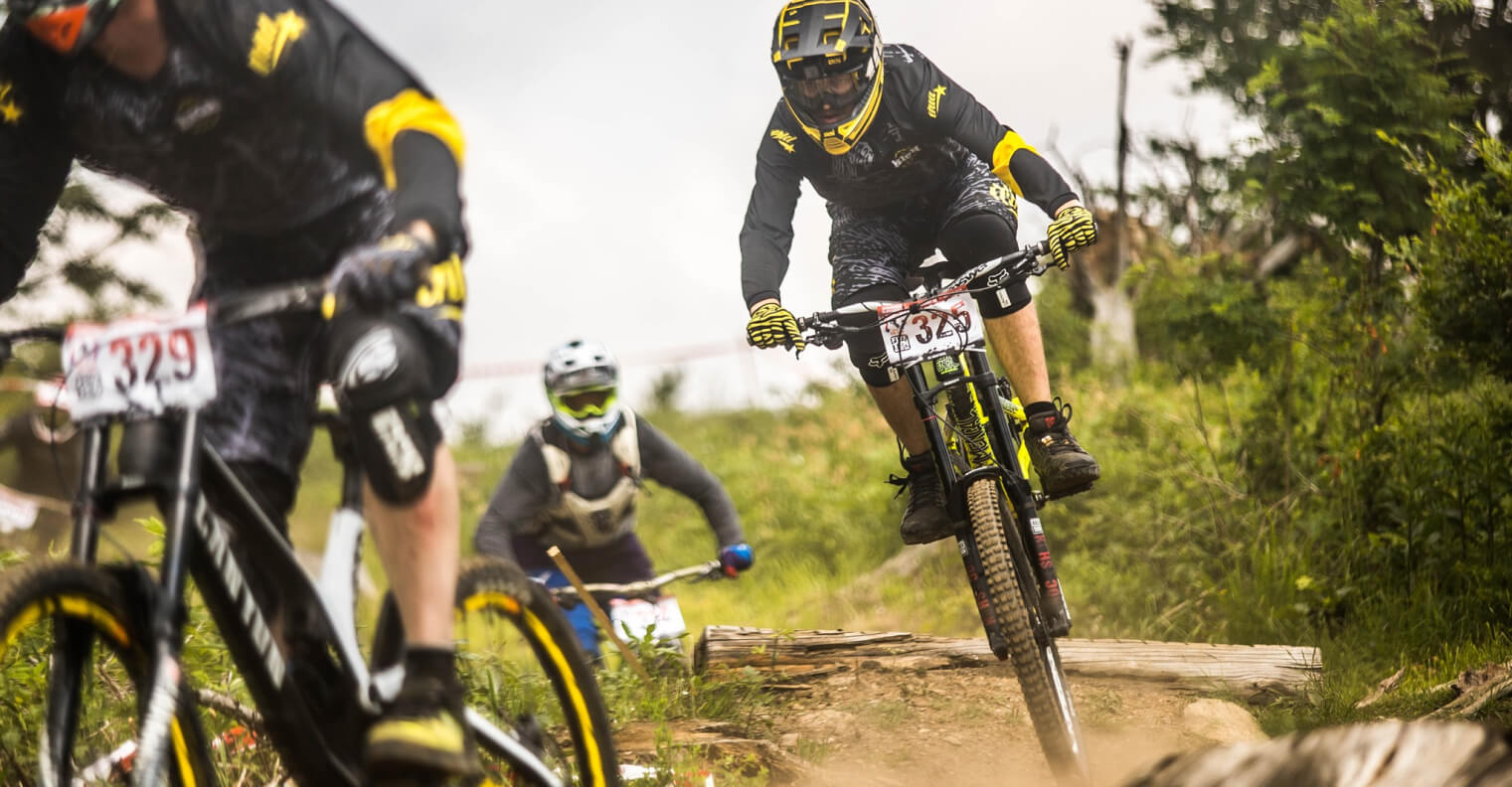 Racers on a dusty downhill track in Too High To Die kit