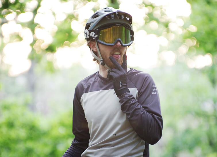 A rider in a Too High To Die jersey wearing a helmet and goggles in the woods