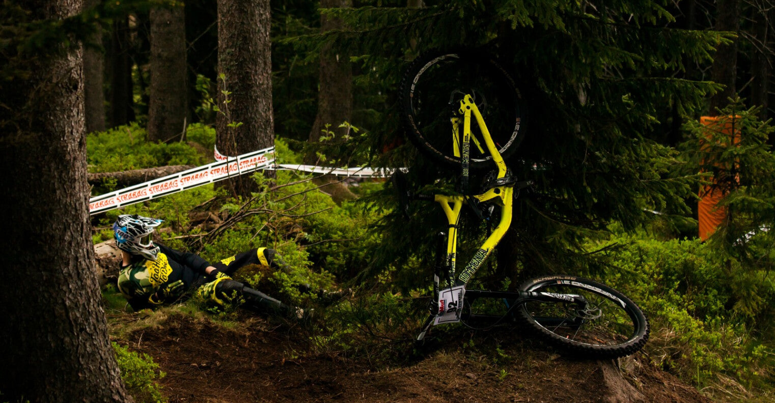 A rider down beside a yellow bike on a forest downhill track
