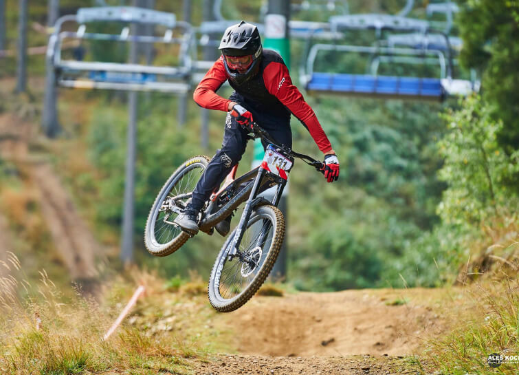 Downhill racer jumping on a track with a chairlift behind